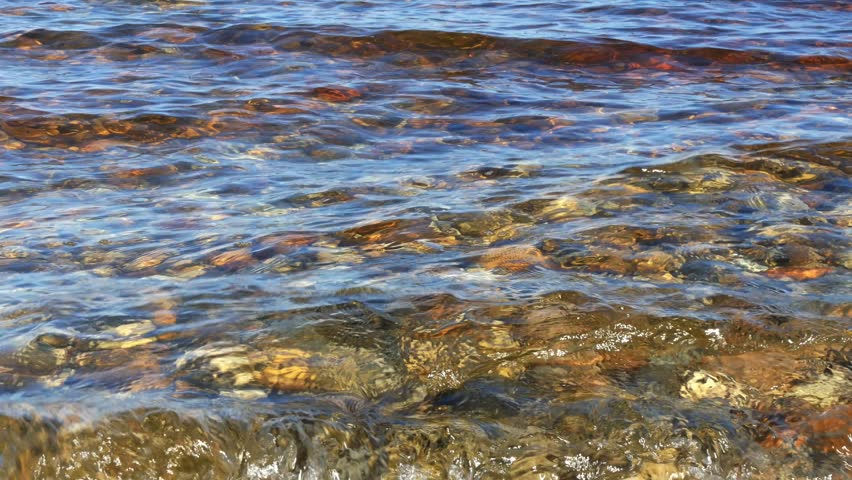 The cold, clear water of Lake Baikal. Through the crystal-clear water, the shoreline, with its colorful rocks and sand, is visible.