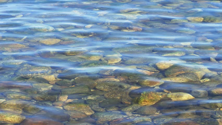 The cold, clear water of Lake Baikal. Through the crystal-clear water, the shoreline, with its colorful rocks and sand, is visible.