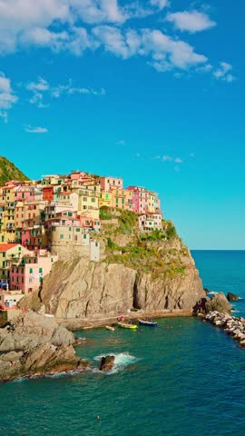 Vertical panoramic shot of Manarola perched on cliffs above blue water in spring sunlight. Commercial use for tourism and destination visuals.