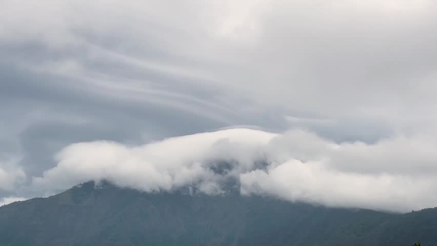 Wide landscape footage of a thick cloud mountain rising above a mist-covered calm volcanic lake