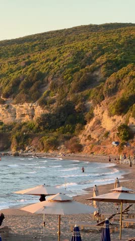 Sunny beach with umbrellas and rocky coastline of the Adriatic Sea in Albania at golden hour