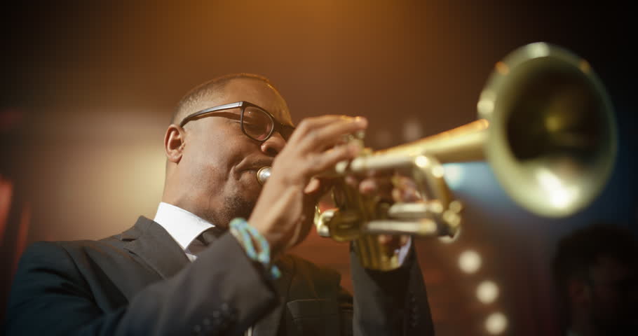 Black Male Trumpet Player Leads a Live Jazz Band Concert in a Bar, Playing an Expressive Song on Stage as the Audience Watches This Intimate Music Event at Stylish Club. Cinematic Handheld