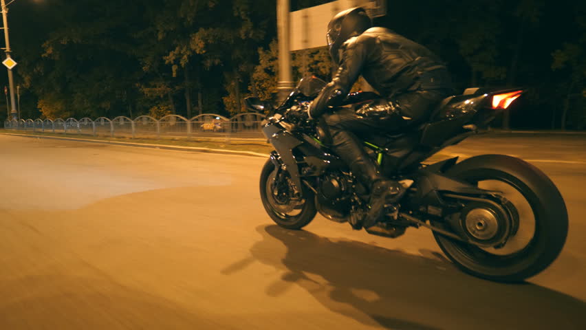 Motorcyclist racing his motorcycle on nighty road. Young man in helmet riding fast on modern sport motorbike at evening street. Guy driving bike at dusk. Concept of freedom and adventure. Side view