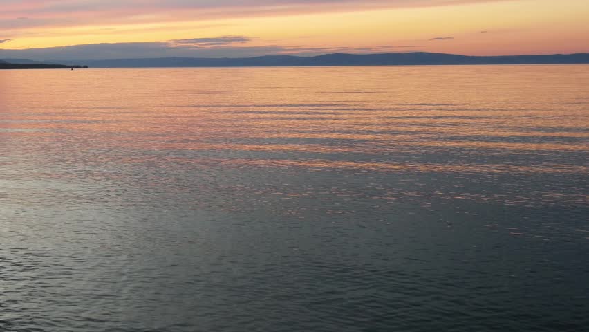 Sunset on Lake Baikal in Russian Siberia on a chilly autumn evening. The orange sky is reflected in the calm surface of the lake.