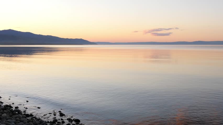 Sunset on Lake Baikal in Russian Siberia on a chilly autumn evening. The orange sky is reflected in the calm surface of the lake.