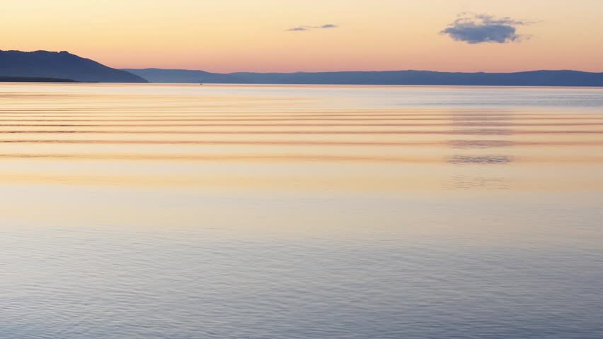 Sunset on Lake Baikal in Russian Siberia on a chilly autumn evening. The orange sky is reflected in the calm surface of the lake.
