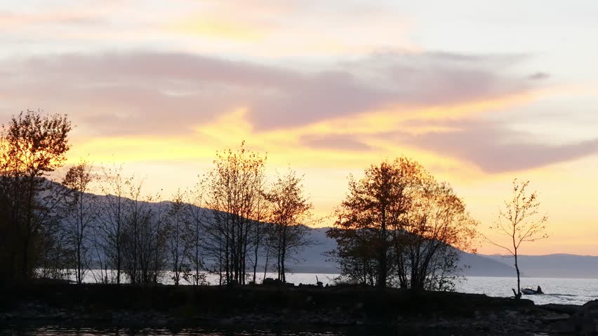 Sunset on Lake Baikal in Russian Siberia on a chilly autumn evening. The orange sky is reflected in the calm surface of the lake.