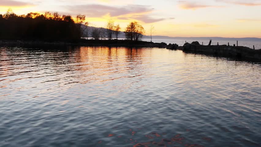 Sunset on Lake Baikal in Russian Siberia on a chilly autumn evening. The orange sky is reflected in the calm surface of the lake.