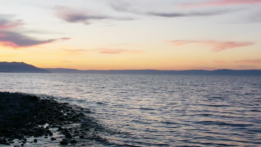 Sunset on Lake Baikal in Russian Siberia on a chilly autumn evening. The orange sky is reflected in the calm surface of the lake.