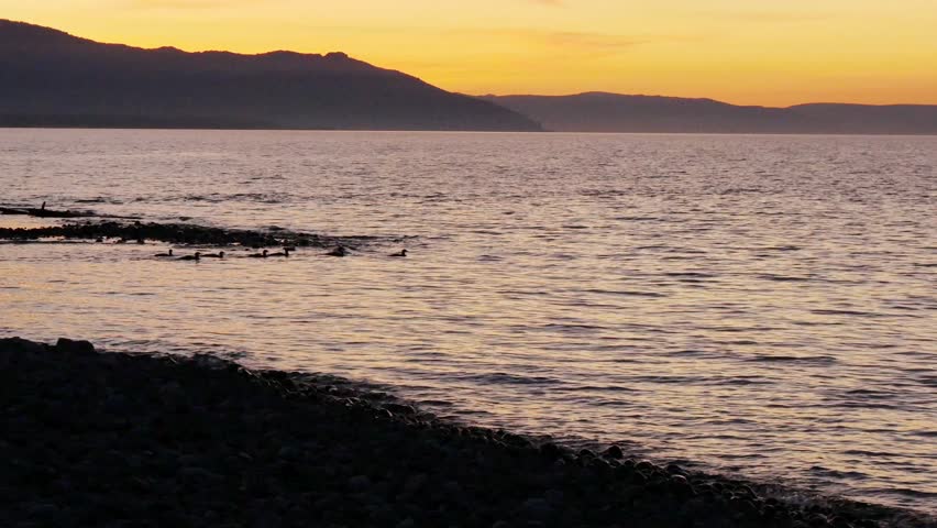 Sunset on Lake Baikal in Russian Siberia on a chilly autumn evening. The orange sky is reflected in the calm surface of the lake.
