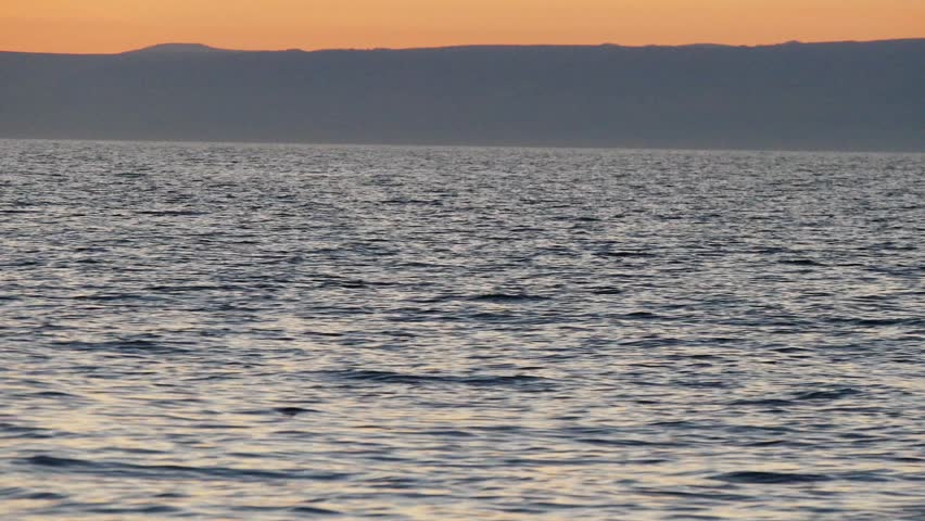 Sunset on Lake Baikal in Russian Siberia on a chilly autumn evening. The orange sky is reflected in the calm surface of the lake.