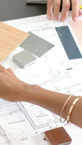 Vertical video: Desk plan urging woman in striped top testing wood tiles to match rooms, copy space. Blueprint, collaboration, industrial, architecture, studio, veneer, vertical video