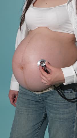 Pregnant woman checking fetal heartbeat with a stethoscope