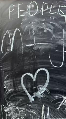 Vertical stock video chalkboard covered with chaotic doodles and smeared hearts, layered scribbles, eraser streaks and loops, closeup texture evokes nostalgic classroom art