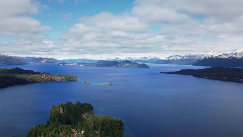 Static afternoon aerial timelapse over Nahuel Huapi lake. Fast-moving stratocumulus clouds project dynamic shadows over the lake and Andes mountains, with changing water textures in Patagonia.