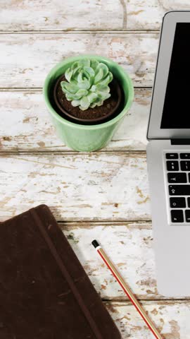 Laptop, pot plant, diary, pencil and mobile phone on wooden surface