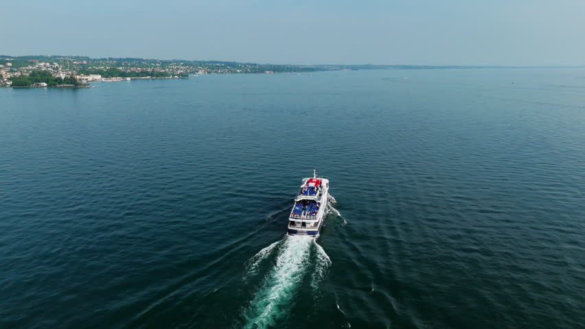 Passenger ferry leaving trail wake on open water of Lake Garda, aerial rear view of transport vessel