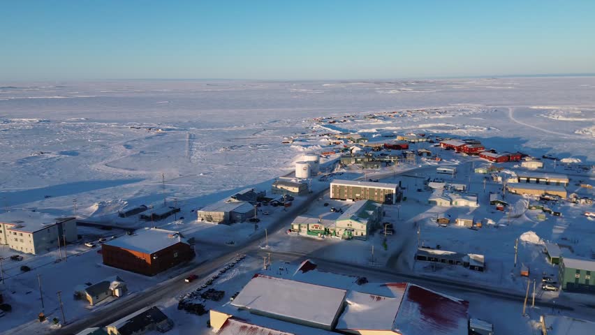 Aerial pan from left to right over the residential housing and frozen tundra of Rankin Inlet (Kangiqliniq) during a golden hour sunset.