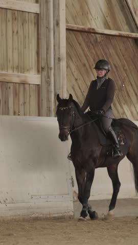 Professional female equestrian training her dark bay horse inside a spacious indoor riding arena