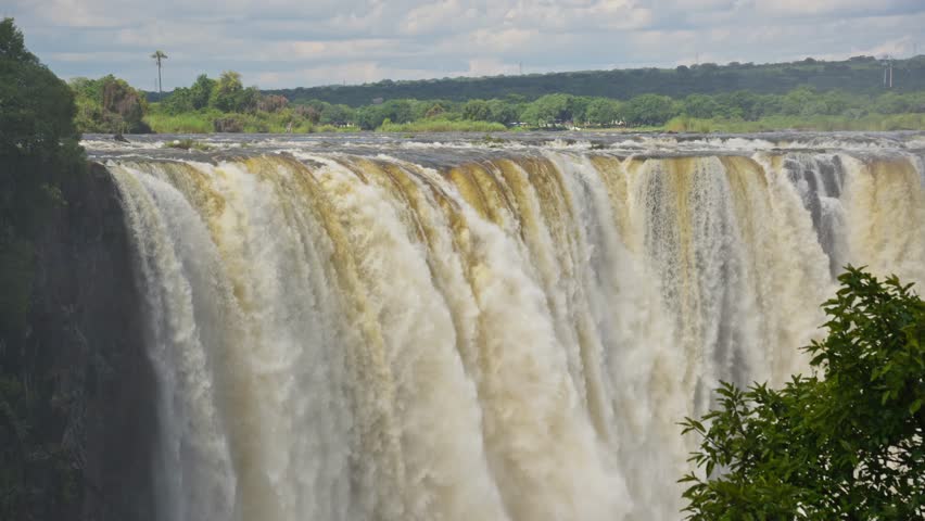 Majestic Victoria Falls powerful cascades of water plunging down basalt cliffs, immense spray and mist over Zambezi River on border of Zambia and Zimbabwe
