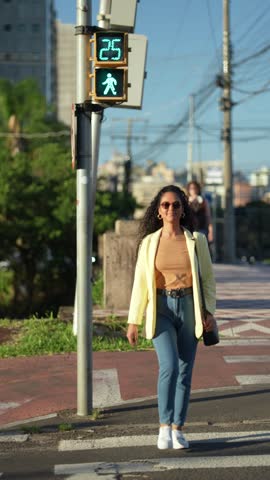 Young Brazilian businesswoman with sunglasses crossing urban street on green pedestrian signal at zebra crosswalk