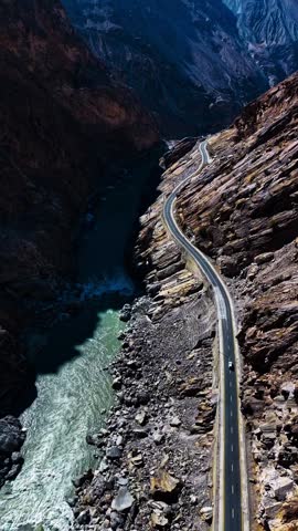 Breathtaking high-angle shot of a winding asphalt road carved into steep cliffs alongside a deep river gorge in a rugged mountain canyon.
