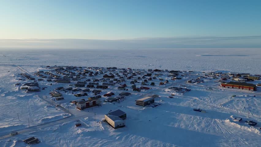 Aerial drone pan left to right over the remote Arctic town of Arviat, Nunavut. Shows colorful northern housing on the flat coastal tundra. A view of community life in the Kivalliq region.