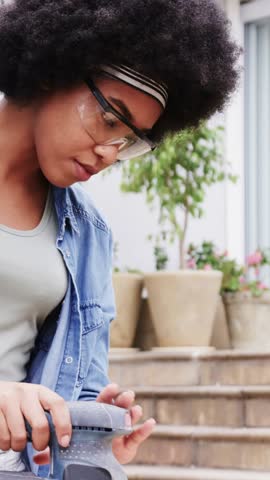 Vertical video: Sanding woman wearing goggles and denim shirt gripping sander on patio for repair. Outdoor, diy, maintenance, focus, terrace, plants, vertical video