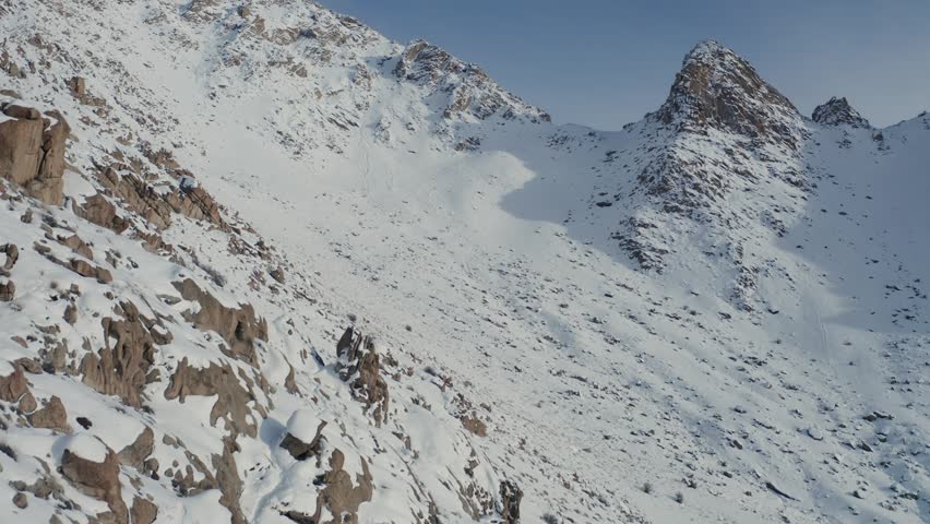 Snow-covered Himalayan mountain peaks with exposed rocky slopes in Ulley, Ladakh, India. Slow forward motion reveals the high-altitude winter landscape under clear blue sky with fresh snow.