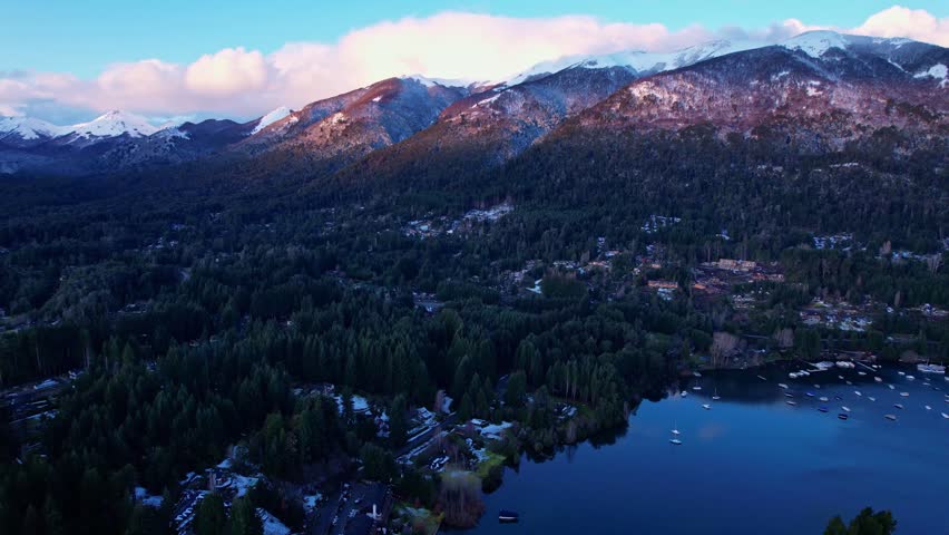 Forward drone dolly in shot at dusk over the dark forest of Puerto Manzano peninsula in Villa La Angostura, Patagonia, Argentina. Andes mountains under a sunset sky.