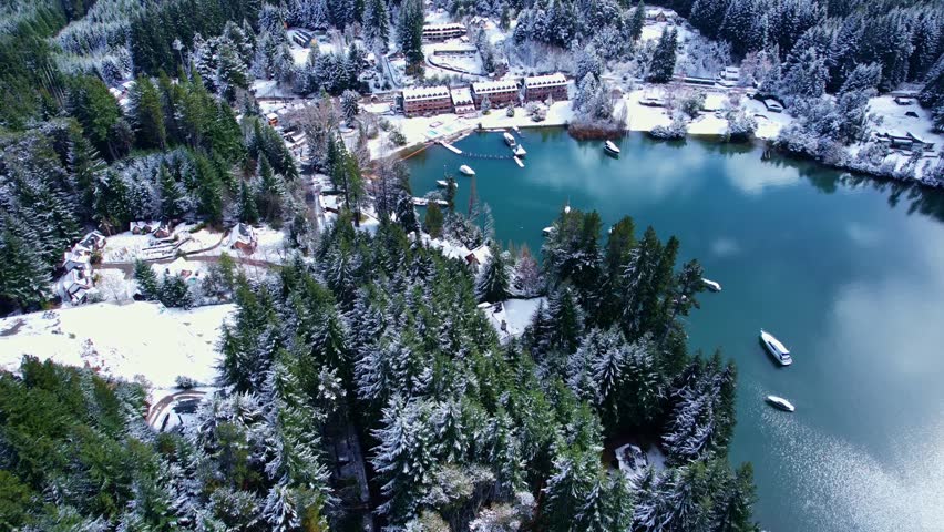 Drone moving forward while tilting camera up to reveal a luxury lakeside resort, moored boats, and the snow-capped Andes mountains on Nahuel Huapi Lake, Patagonia National Park.