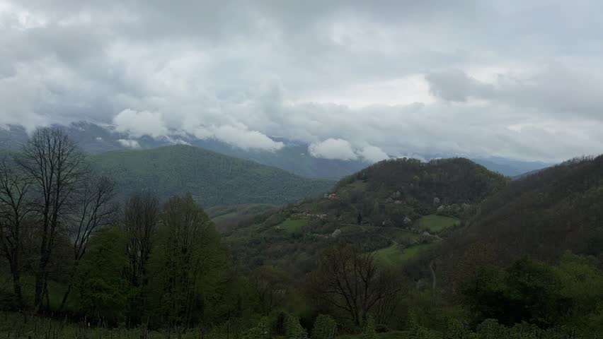 Time lapse of clouds drifting over green mountain landscape with rolling hills and forest. Dynamic sky and changing weather in natural environment. Scenic countryside view with atmospheric motion.