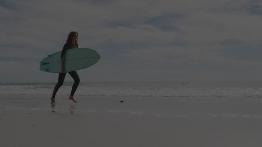 Woman surfer entering left moving right with board radial burst growing hiding form heading to surf. Beach, wetsuit, silhouette, motion, ocean, horizon, overcast