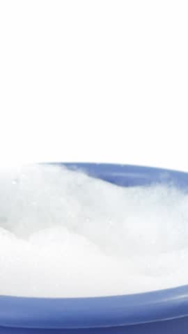 Cleaning sponge falling in to bucket of soap suds against white background