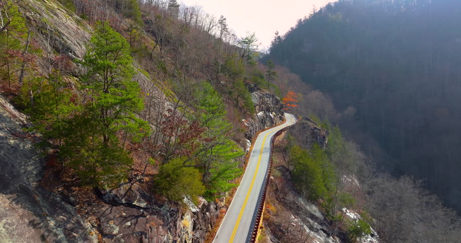 Car driving along Highlands Road, a scenic mountain pass in North Carolina. Steep rocky hillsides and vibrant fall foliage line the route
