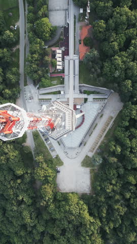 High-altitude vertical drone shot of the Avala Tower in Belgrade, Serbia, surrounded by dense greenery.