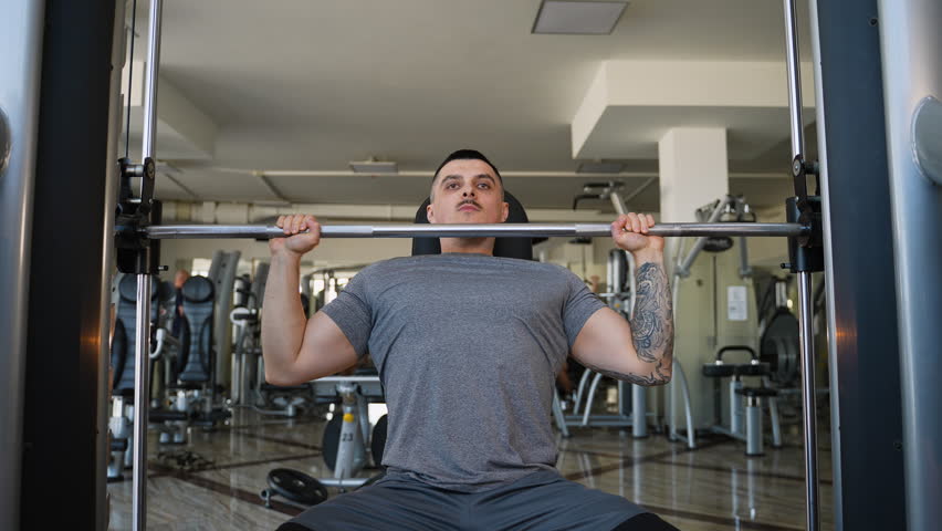 Tattooed muscular man lifting barbell in gym