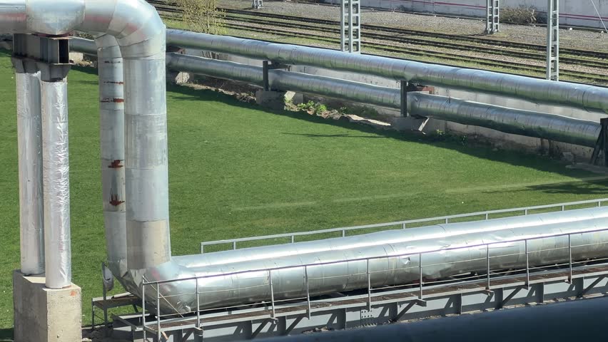Large metal pipes are placed on a grassy area next to the railway tracks.