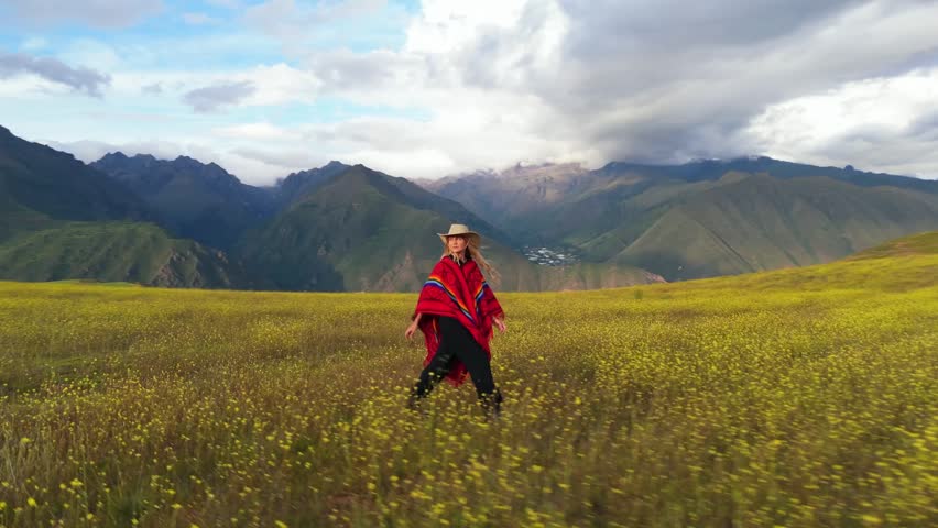Aerial view of a woman in traditional Peruvian attire walking through a vibrant yellow field in the Andes