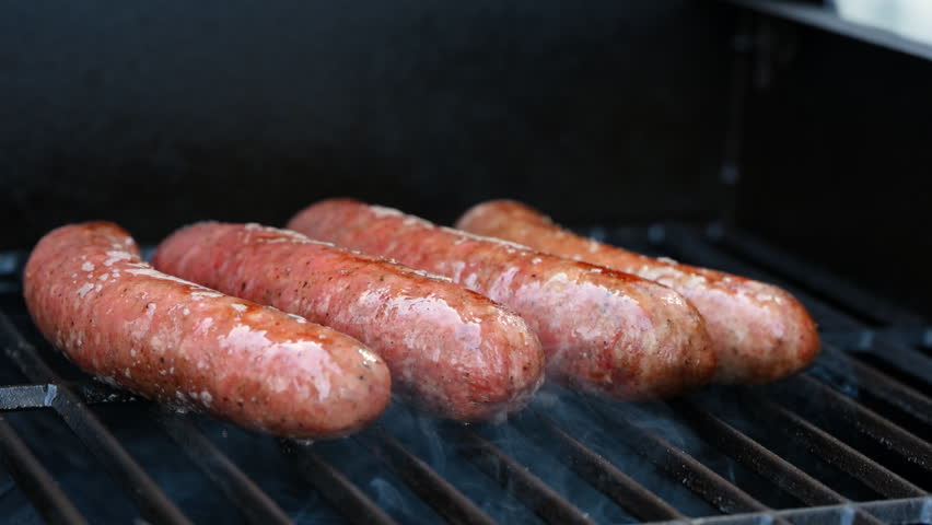 View of raw sausages grilling on barbecue with open flame. Close up of juicy meat cooking on grill, outdoor food and summer barbecue