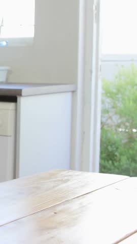 Vertical video: Woman sitting kitchen, alerts popping, counts up, smiling, taking phone for ads. Tabletop, smartphone, notifications, adult, window, garden, vertical video