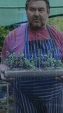 Vertical video: Senior gardener nodding as cam moving down holding tray checking sprouts with tints. Seedlings, planter, canopy, nursery, greenhouse, elderly, vertical video - Powered by Shutterstock - Get 15% off with code: PIKWIZARD15