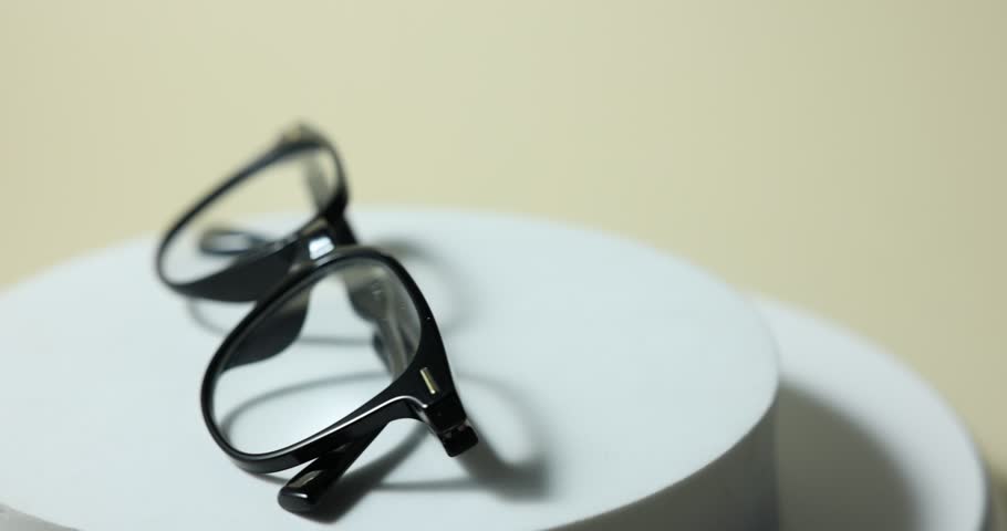 Pair of stylish eyeglasses on podium against light background, rotating