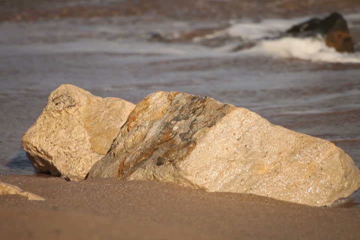 Waves wash shore sands. Foreground rock.
