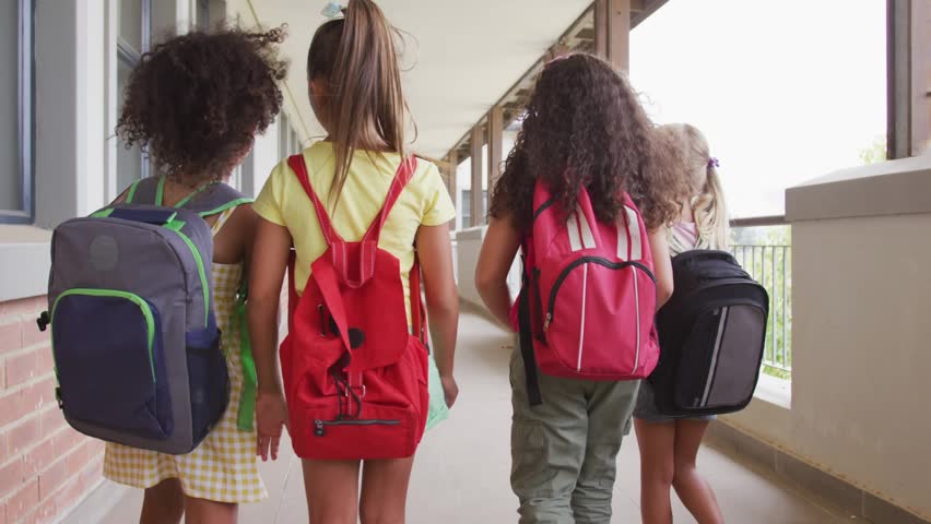 Four students walking school after class, backpacks, one holding bottle, blue overlay across frame. Group, girls, corridor, friendship, outdoors, education, candid