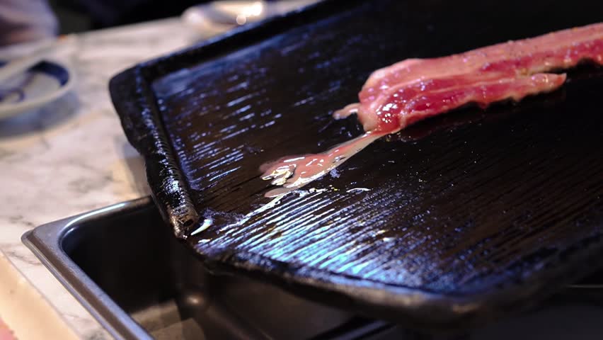 The moment of Korean bbq grilling pork belly with fat dripping on a hot iron plate