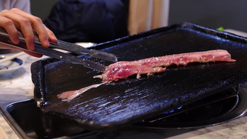 Woman grilling Korean bbq Samgyeopsal with tong in a Korean restaurant