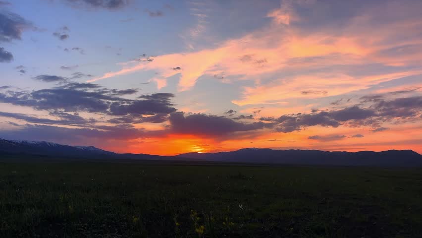 Beautiful orange sunset sky over the vast green grassland and distant mountain range in Xinjiang China.