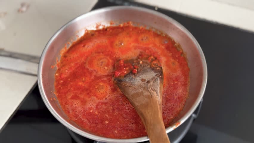 Spicy chili sauce simmering in a pan while being stirred during cooking.