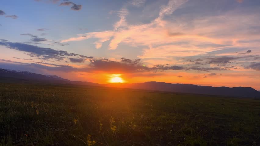 Stunning orange sunset with wispy clouds over the green plains and distant mountains in Xinjiang China.